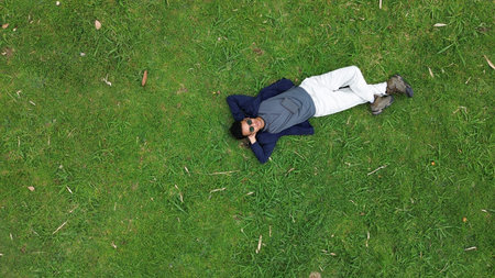 A man is laying on the grass, holding a cell phone. The scene is peaceful and relaxing, with the man...