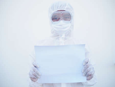 Young doctor or scientist in PPE suite uniform holding blank paper for text with both hands While looking ahead. coronavirus or COVID-19 concept isolated white backgroundの写真素材