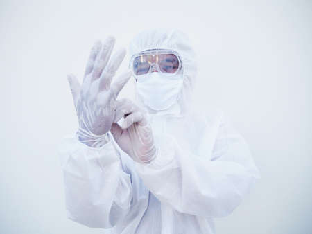 Asian doctor or scientist in PPE suite uniform putting on protective white gloves while looking hands.  COVID-19 concept isolated white backgroundの写真素材