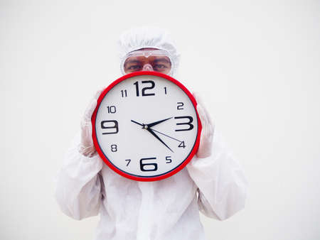 Portrait of doctor or scientist in PPE suite uniform holding red alarm clock and looking at the camera In various gestures. COVID-19 concept isolated white backgroundの写真素材