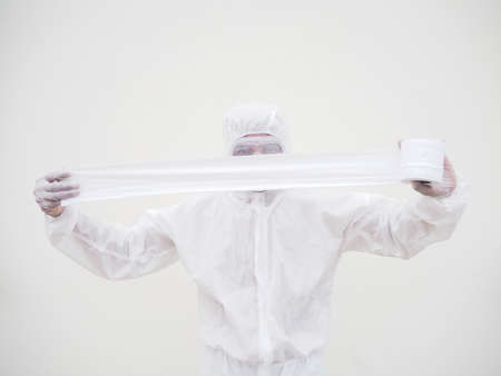 Asian male doctor or scientist in PPE suite uniform holding toilet paper. Lack of toilet paper in the quarantine of coronavirus. COVID-19 concept isolated white backgroundの写真素材