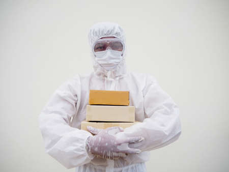 Young man in PPE suite uniform while holding cardboard boxes in medical rubber gloves and mask....