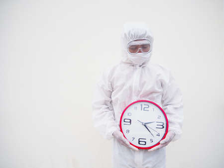 Portrait of doctor or scientist in PPE suite uniform holding red alarm clock and looking to the down In various gestures. COVID-19 concept isolated white backgroundの写真素材