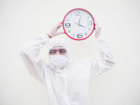 Portrait of doctor or scientist in PPE suite uniform holding red alarm clock and looking at the camera In various gestures. COVID-19 concept isolated white backgroundの写真素材