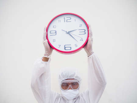 Portrait of doctor or scientist in PPE suite uniform holding red alarm clock and looking at the camera In various gestures. COVID-19 concept isolated white backgroundの写真素材