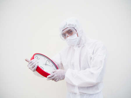Portrait of doctor or scientist in PPE suite uniform holding red alarm clock and looking at the...