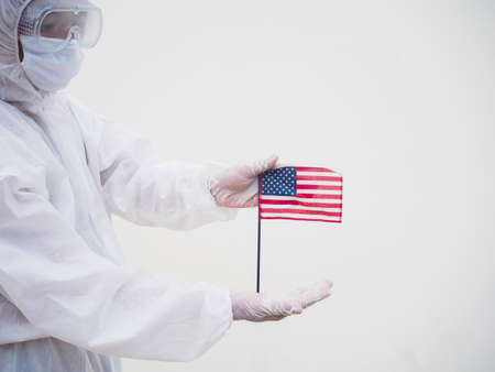 Portrait of doctor or scientist in PPE suite uniform holding national flag of United states of America. COVID-19 concept isolated white backgroundの写真素材