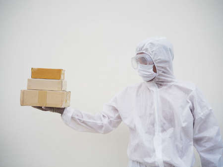 Young man in PPE suite uniform while holding cardboard boxes in medical rubber gloves and mask....