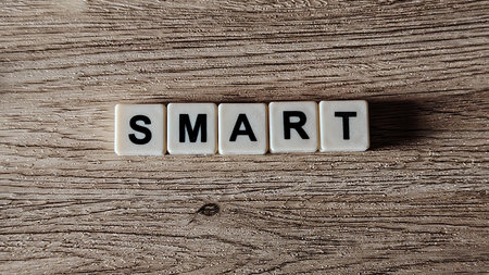 A top-down view of the word "SMART" spelled with letter tiles in a straight line on a highly textured wooden background.の写真素材