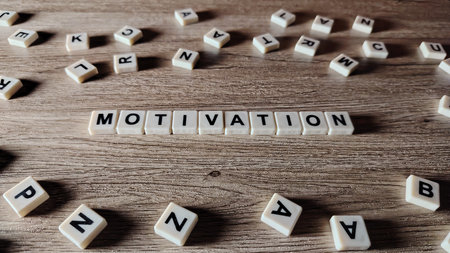 The word "MOTIVATION" spelled out in a line with letter tiles on a wooden texture background, with other letters scattered around.の写真素材