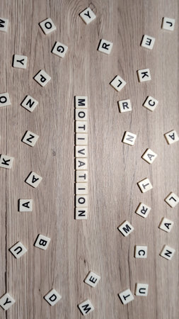 A flat lay top view of "MOTIVATION" in letter tiles, centered on a wooden background and encircled by randomly scattered letters.の写真素材