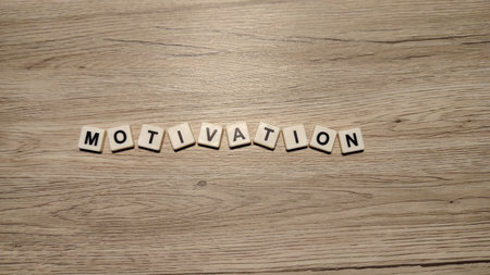 The word "MOTIVATION" spelled with letter tiles in a single line, centered on a minimalist wood grain textured background.の写真素材