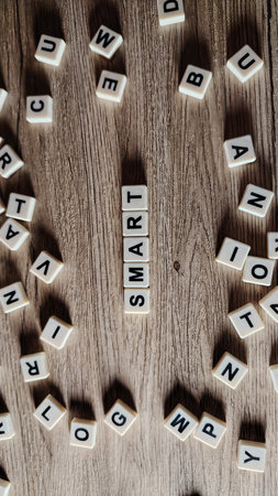 The word "SMART" spelled with letter tiles, centered on a wooden background and surrounded by scattered alphabet blocks.の写真素材