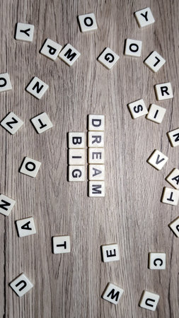 The motivational phrase "DREAM BIG" in letter tiles, centered on a wood background and loosely framed by scattered letters. Flat lay.の写真素材
