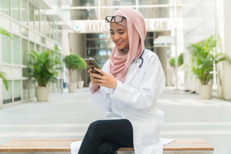 Beautiful Malay lady Doctor wearing glasses and stethoscope holding mobile phoneの写真素材