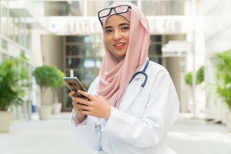 Beautiful Malay lady Doctor wearing glasses and stethoscope holding mobile phoneの写真素材