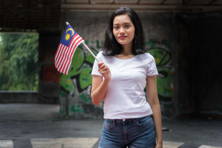 Asian Girl Wearing Plain White Cloth Outdoor holding Malaysian Flagの写真素材
