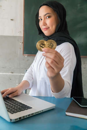 Happy young woman wearing hijab Holding Bitcoin Money using Laptopの写真素材