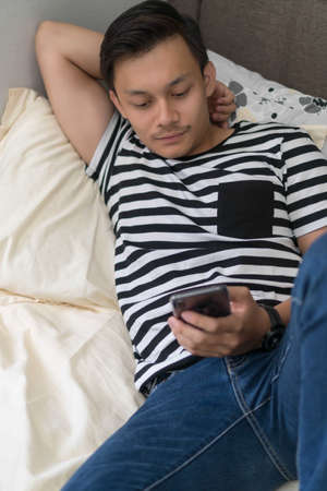 Relaxed casual man using a smart phone lying on the bed at homeの写真素材