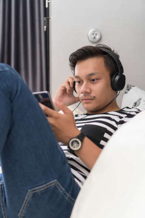 Relaxed casual man using a smart phone lying on the bed at homeの写真素材