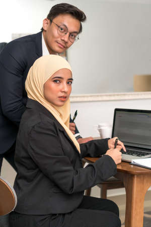 Asian malay executive working at home with laptop looking at the camera
