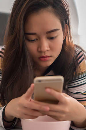 Beautiful young Asian girl on the bed holding mobile phone