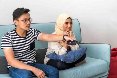 Young Malay Couple at the Sofa watching tv together holding remote