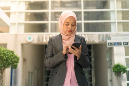Asian Business Women wearing hijab smiling while using mobile phoneの写真素材