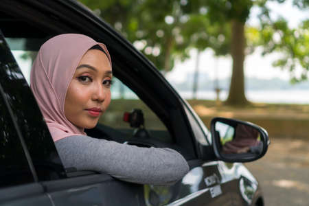 Cute Asian girl wearing hijab looking thru car windowsの写真素材
