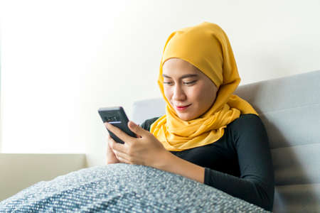 Asian Malay girl wearing hijab sitting in the sofa alone using smart phone
