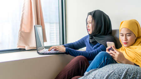 Two friends in the room using laptop and playing with smartphone