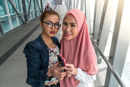 Two friends at the train station holding smartphone, telecommunication conceptの写真素材