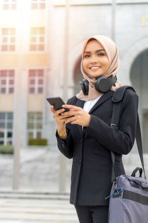 Office concept, malay woman wearing suit and laptop bag walking while holding smartphoneの写真素材