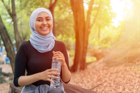 Healthy Lifestyle Concept, Malay Muslim lady wearing hijab outdoor resting and drink waterの写真素材