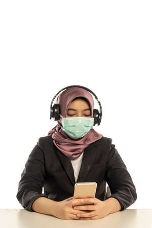 Business Lifestyle, Cute Malay Woman wearing hijab and facemask listening to the musicの写真素材