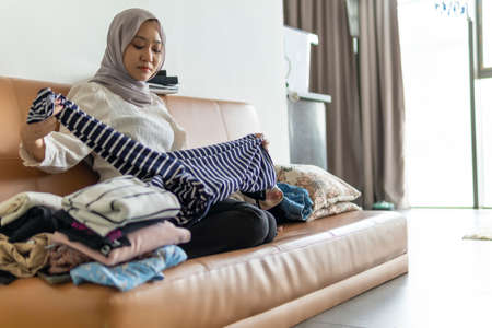 Lifestyle at home, cute malay woman doing routine housework by folding her laundry