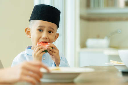 Eid Mubarak celebration moment, little boy eating fruits. Malaysian people wearing traditional clothの写真素材