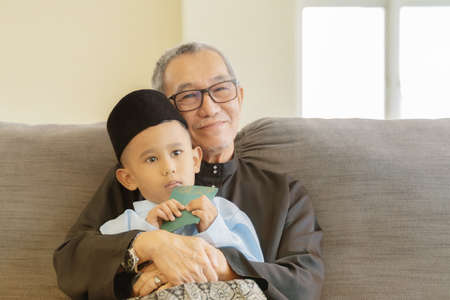 Eid Mubarak celebration moment, grand father with grand son wearing traditional cloth at the sofa.の写真素材
