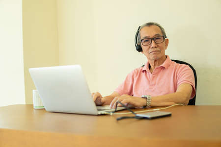 Technology concept, senior citizen using laptop at home. Work from home sitting at the work desk for conference callの写真素材