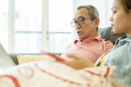 Father and daughter concept, senior citizen using laptop at home sitting at the sofa with his daughterの写真素材