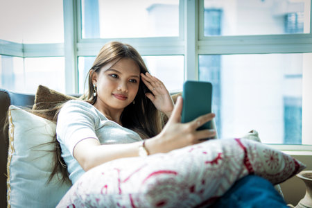 Online Dating Concept, Beautiful Asian girl at the sofa using smartphoneの写真素材