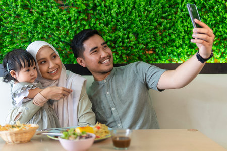 Family moment: Young couple with toddler at the restaurant taking selfie with smart phoneの写真素材