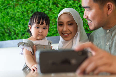 Family moment: Young couple with toddler at the restaurant taking selfie with smart phoneの写真素材