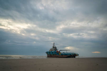 Kuantan, Pahang, Malaysia - March 9 2022 - Stranded tug boat at the shore with cloudy sunrise in the morningのeditorial素材