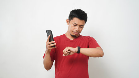 Young Asian man wearing red t-shirt using smart watch on white background.の写真素材