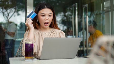 Young beautiful asian woman using using laptop and holding credit card with shocked or surprised...