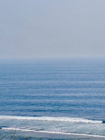 The calm ocean horizon stretches endlessly, where the tranquil blue of the sea meets the delicate pastel hues of the sky. Gentle waves ripple softly under a golden sun, casting a serene shimmerの写真素材