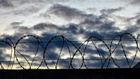 Close-up of metal fence with barbed wire over a dramatic sky