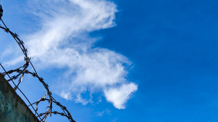 Close-up of metal fence with barbed wire over a dramatic sky