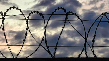 Close-up of metal fence with barbed wire over a dramatic skyの写真素材